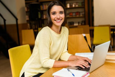 Resim kitaplığındaki okumak ev ödevi eğitim ve dizüstü bilgisayar kullanan bir genç öğrenci mutlu kadın.