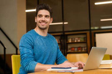 Genç öğrenci mutlu bir adam okumak ev ödevi eğitim ve dizüstü bilgisayar kullanan kitaplığındaki görüntü.