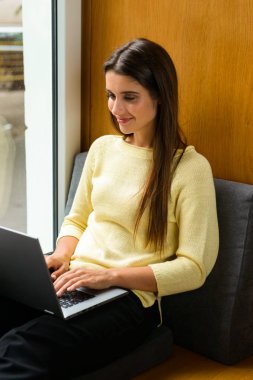 Resim kitaplığındaki dizüstü bilgisayar kullanan bir genç öğrenci konsantre kadının.