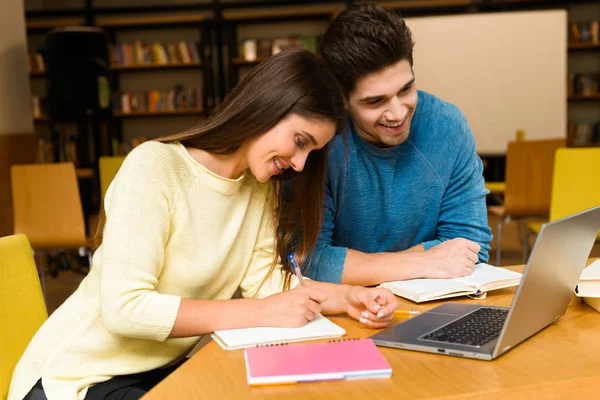 Genç öğrenciler arkadaş çift okumak ev ödevi eğitim ve dizüstü bilgisayar kullanan Kitaplığı'nda.