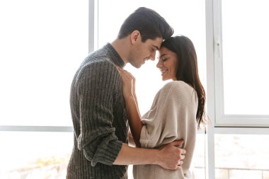 Mutlu genç çift evde pencereden dururken sarılma