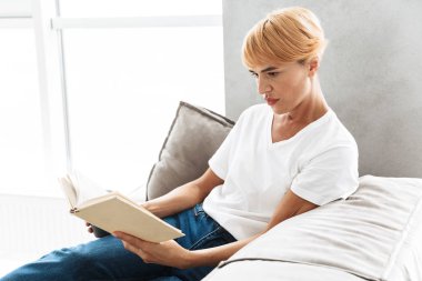 Çekici genç kadın evde bir kanepede otururken kitap okuma