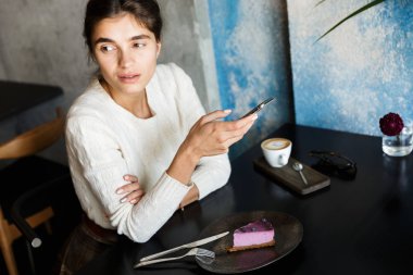 Kapalı cep telefonu sohbet kullanarak Cafe içme kahve oturan genç ve güzel kadın görüntüsünü.