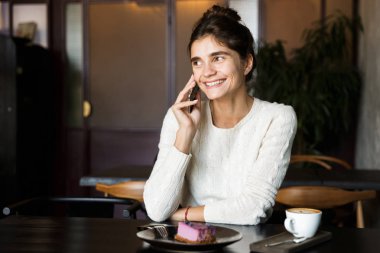 Kapalı cep telefonu konuşurken kullanarak Cafe içme kahve oturan mutlu genç kadın görüntüsünü.