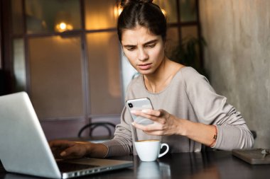 Kapalı dizüstü bilgisayar ve cep telefonu kullanarak kafede oturan genç ve güzel kadın görüntüsünü.