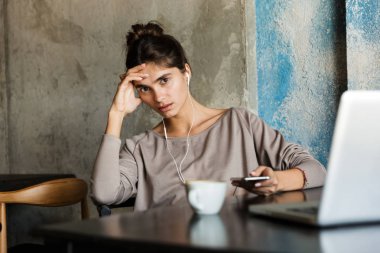 Kapalı dizüstü bilgisayar ve cep telefonu kullanarak kafede oturan oldukça ciddi genç kadın fotoğrafı.