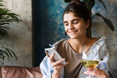 Kapalı cep telefonu kullanarak beyaz şarap içme kafede otururken çok güzel genç kadın fotoğrafı.