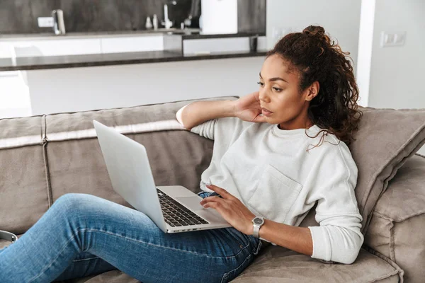 Foto Glada Afroamerikanska Kvinna Använder Laptop Liggandes Soffan Ljust Vardagsrum — Stockfoto