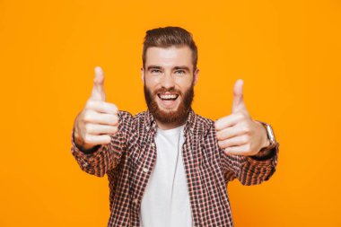 Yaşasın vererek sarı arka plan üzerinde izole ayakta rahat kıyafetler giymiş neşeli genç bir adam portresi