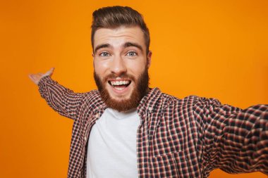 Bir selfie alarak sarı arka plan üzerinde izole ayakta rahat kıyafetler giymiş neşeli genç bir adam portresi