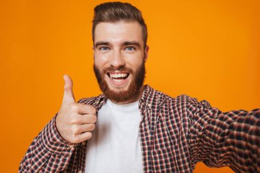 Bir selfie alarak sarı arka plan üzerinde izole ayakta rahat kıyafetler giymiş neşeli genç bir adam portresi