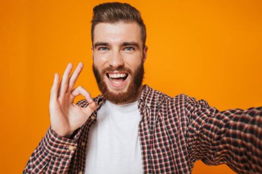 Bir selfie alarak sarı arka plan üzerinde izole ayakta rahat kıyafetler giymiş neşeli genç bir adam portresi