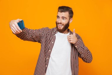 Bir selfie alarak sarı arka plan üzerinde izole ayakta rahat kıyafetler giymiş neşeli genç bir adam portresi