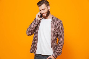 Cep telefonu üzerinde konuşurken sarı arka plan üzerinde izole ayakta rahat kıyafetler giymiş neşeli genç bir adam portresi