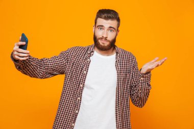 Bir selfie alarak sarı arka plan üzerinde izole ayakta rahat kıyafetler giymiş karışık genç bir adam portresi