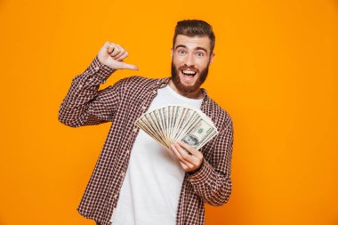 Para banknot gösterilen, parmak işaret sarı arka plan üzerinde izole ayakta rahat kıyafetler giymiş neşeli genç bir adam portresi