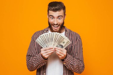 Para banknot gösterilen sarı arka plan üzerinde izole ayakta rahat kıyafetler giymiş neşeli genç bir adam portresi