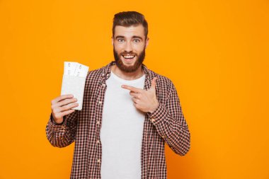 Passport uçak biletleri ile gösterilen sarı arka plan üzerinde izole ayakta rahat kıyafetler giymiş neşeli genç bir adam portresi