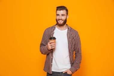 Paket servisi olan restoran kahve tutan sarı arka plan üzerinde izole ayakta rahat kıyafetler giymiş neşeli genç bir adam portresi
