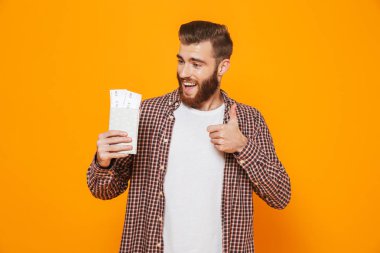 Passport uçak biletleri ile gösterilen sarı arka plan üzerinde izole ayakta rahat kıyafetler giymiş neşeli genç bir adam portresi