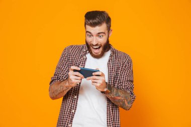 Cep telefonu oyunları oynamak sarı arka plan üzerinde izole ayakta rahat kıyafetler giymiş neşeli genç bir adam portresi