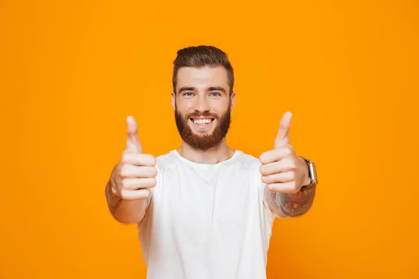 Portrait of a cheerful young man wearing casual clothes standing isolated over yellow background, giving thumbs up