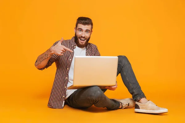 一个开朗的年轻人的肖像 穿着休闲的衣服 坐在孤立的黄色背景 拿着笔记本电脑 — 图库照片