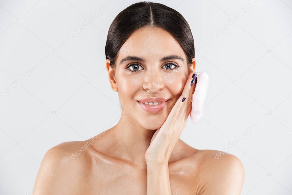 Beauty portrait of an attractive healthy woman standing isolated over white background, using powder puff