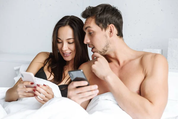 Beau Jeune Couple Couché Lit Tenant Des Téléphones Mobiles — Photo