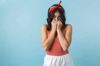 Mavi arka plan üzerinde izole ayakta yazlık giysiler giyen çekici mutsuz genç kadın