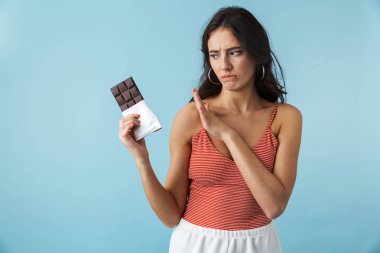 Çikolata bar tutan mavi arka plan üzerinde izole ayakta yazlık giysiler giyen güzel hayal kırıklığına kız