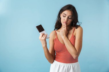 Çikolata bar tutan mavi arka plan üzerinde izole ayakta yazlık giysiler giyen güzel hayal kırıklığına kız