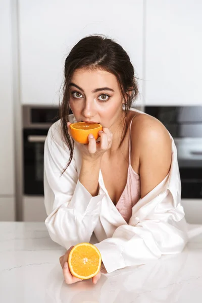 キッチンでオレンジのシルク レジャー服持株 枚身に着けている 代の若い女性の画像 — ストック写真