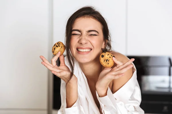 朝食時にキッチンでクッキーを保持している女性 代着用シルク レジャー服の笑顔写真 — ストック写真