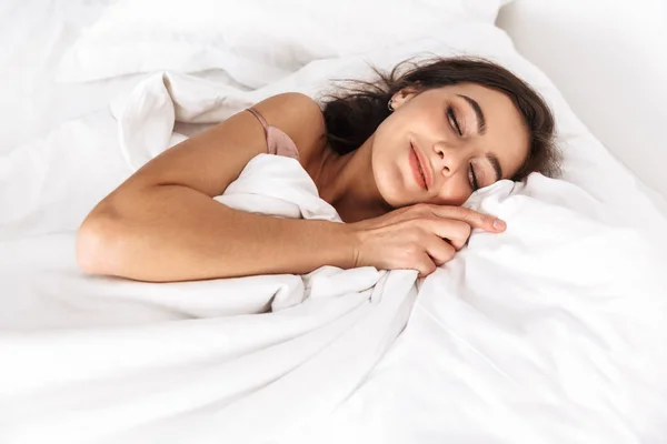睡眠や昼寝の後白い枕の上のベッドに横たわっている間黒い髪を笑顔で満足して女性 代の写真 — ストック写真