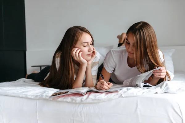 Twee vrolijke jonge tienermeisjes tot op bed, lezen — Stockfoto