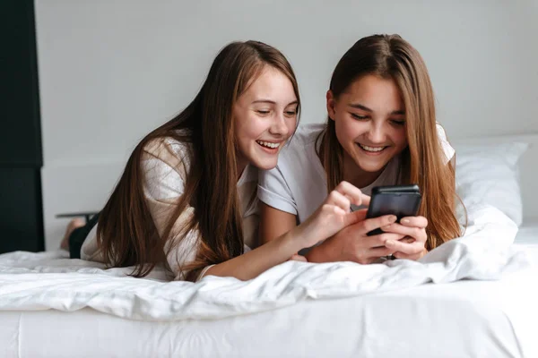 Дві веселі молоді дівчата-підлітки використовують мобільний телефон — стокове фото