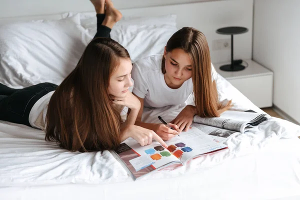 Дві веселі молоді дівчата-підлітки лежать на ліжку, читаючи — стокове фото