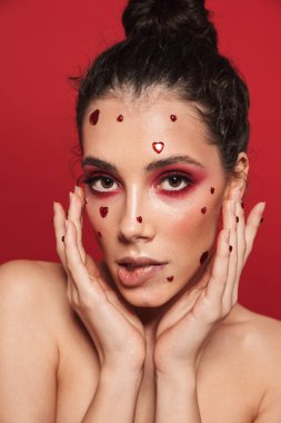 Kadının yüzündeki yürekleri poz kırmızı duvar arka plan üzerinde izole kırmızı parlak makyaj ile.