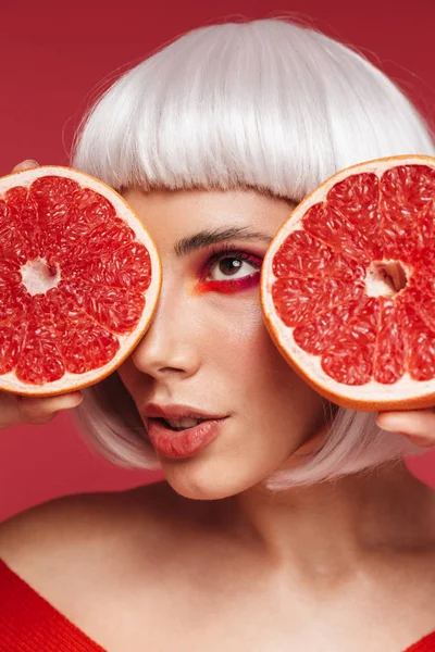 Hermosa joven aislada sobre fondo de pared roja sosteniendo pomelo . — Foto de Stock