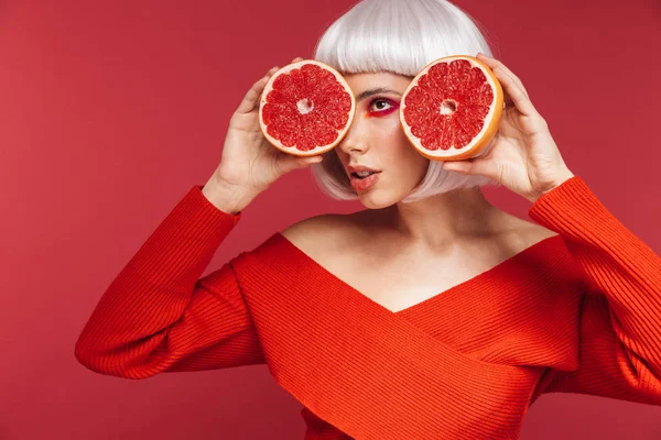 Красивая молодая женщина, изолированная на фоне красной стены с грейпфрутом . — стоковое фото