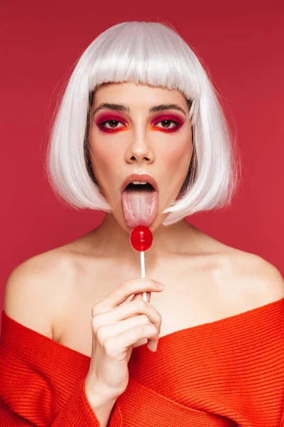 Vacker ung kvinna isolerade över röda väggen bakgrund håller lollipop godis. — Stockfoto