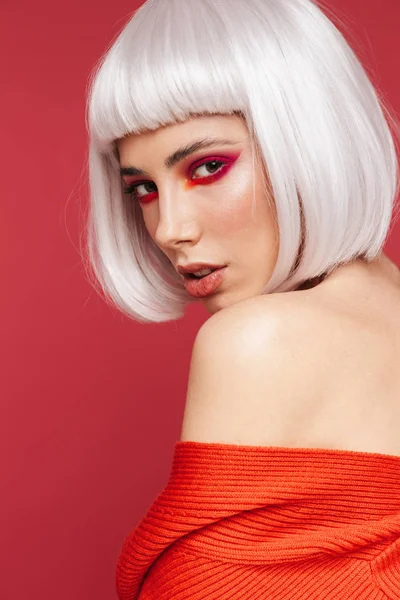 Piękna młoda kobieta na białym tle czerwone ściany ze stawianiem jasny makijaż. — Zdjęcie stockowe
