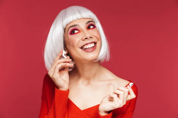Žena izolována červená stěna pozadí s světlý make-up poslechu hudby pomocí sluchátek. — Stock fotografie