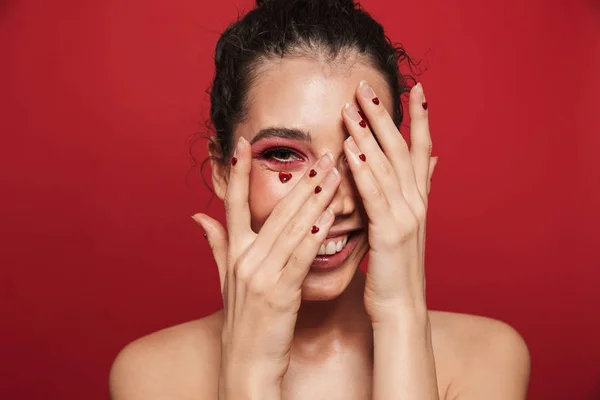 Bella felice allegra giovane donna con rosso trucco luminoso isolato su sfondo muro rosso in posa con i cuori sul viso . — Foto Stock