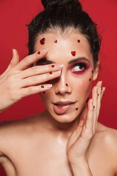 Kadının yüzündeki yürekleri poz kırmızı duvar arka plan üzerinde izole kırmızı parlak makyaj ile. — Stok fotoğraf