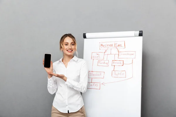 Business woman isolated over grey wall background near desk showing display of mobile phone. — Stock Photo, Image