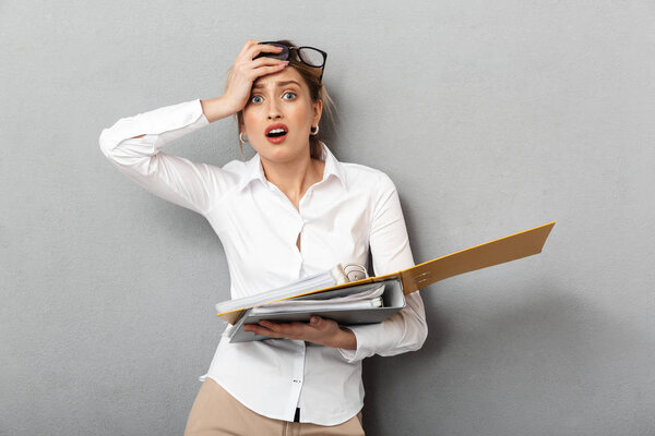 Confused business woman isolated over grey wall background holding folders.