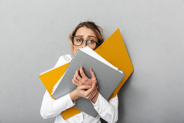 Confused business woman isolated over grey wall background holding folders.
