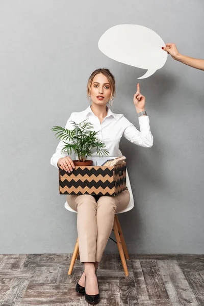 Mulher de negócios isolada sobre fundo de parede cinza segurando caixa com planta e documentos apontando para bolha de fala . — Fotografia de Stock